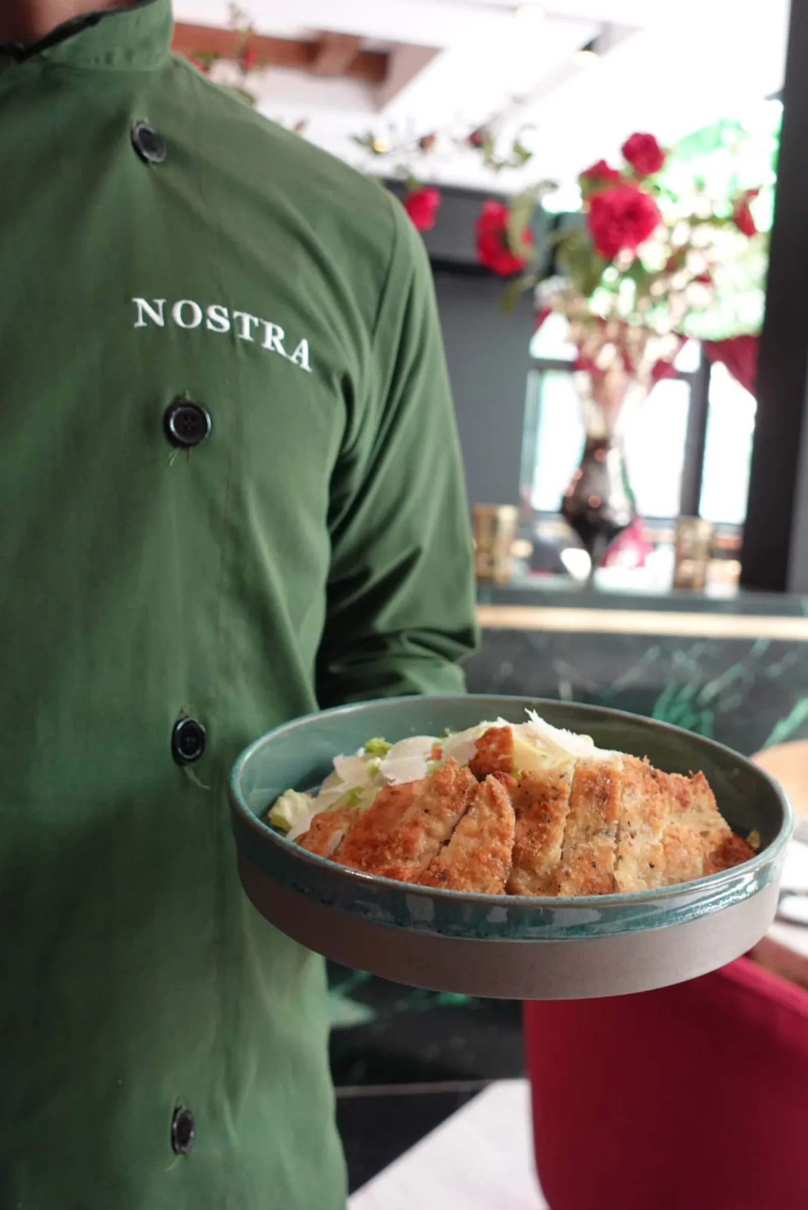 Serveur en veste Nostra présentant un plat, broderie NOSTRA visible